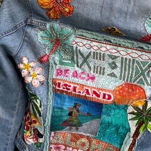 May include: Denim jacket with colorful embroidered patches. Features a large orange hibiscus flower, tropical scenes, and the words "Beach Island" and "Aloha". The jacket has a vintage, handcrafted aesthetic.