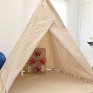 Puede incluir: Una tienda de campa&ntilde;a tipi de lona blanca con una unidad de calefacci&oacute;n roja y negra en su interior. La tienda de campa&ntilde;a est&aacute; montada sobre un suelo marr&oacute;n claro.