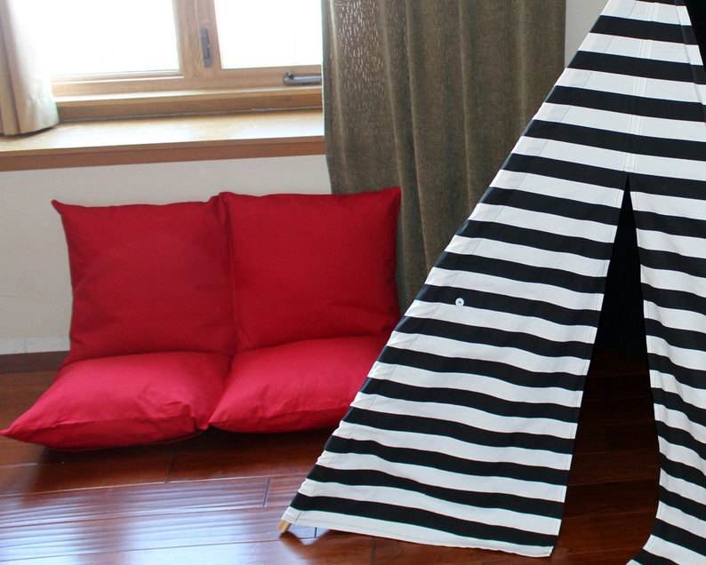 May include: A red floor lounger and a black and white striped teepee are set up indoors. The lounger is made of two square cushions. The teepee has a button closure and wooden poles.