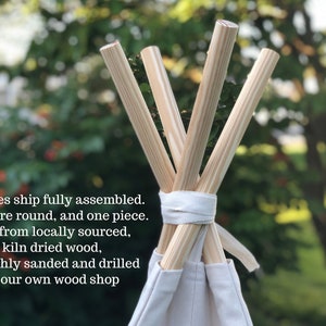 May include: Close-up of the top of a teepee tent with wooden poles. The poles are round and smooth, and they are tied together with a white fabric strap. The teepee is made of white canvas.