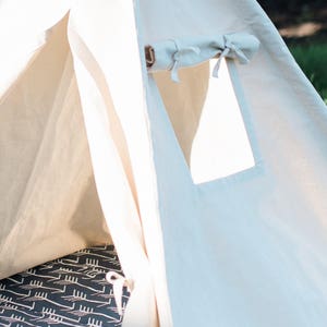 May include: A white canvas teepee tent with a flap opening and a small window. The interior of the tent has a black and white patterned floor mat.