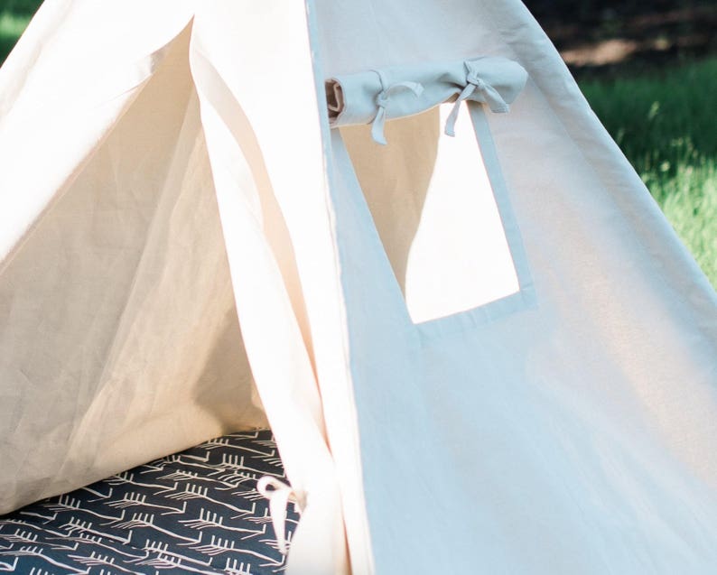 May include: A white canvas teepee tent with a flap opening and a small window. The interior of the tent has a black and white patterned floor mat.