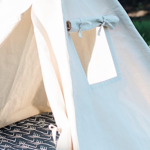 May include: A white canvas teepee tent with a flap opening and a small window. The interior of the tent has a black and white patterned floor mat.