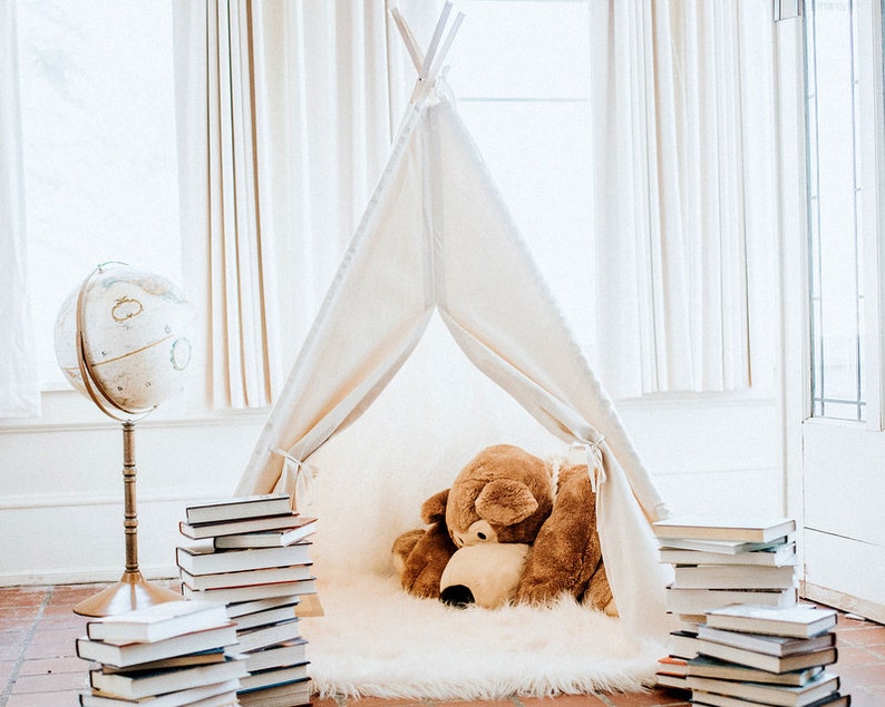 May include: A white teepee tent with a brown stuffed animal inside. The teepee is surrounded by stacks of books and a globe on a stand.