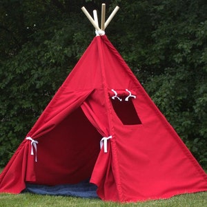 May include: A red canvas teepee tent for kids with white ties and a window. The teepee is set up on a grassy lawn.