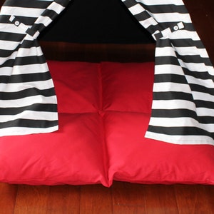 May include: A child's play tent with a black and white striped canopy and a bright red floor cushion. The tent has a teepee shape and is set on a wooden floor.