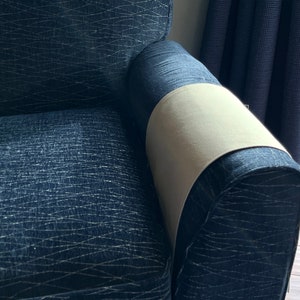 Peut inclure: Un fauteuil bleu fonc&eacute; recouvert d'un tissu &agrave; motif de lignes entrecrois&eacute;es claires. Une housse en tissu beige clair uni est pos&eacute;e sur le dessus de l'accoudoir droit, contrastant avec le rev&ecirc;tement textur&eacute; bleu fonc&eacute; du fauteuil.