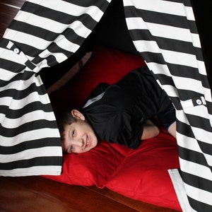 May include: A black and white striped play tent with a red pillow inside. The tent is made of fabric and has a simple design. The tent is set up on a wooden floor.