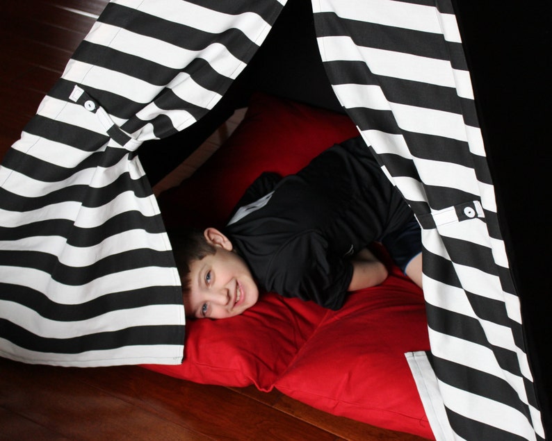 May include: A black and white striped play tent with a red pillow inside. The tent is made of fabric and has a simple design. The tent is set up on a wooden floor.
