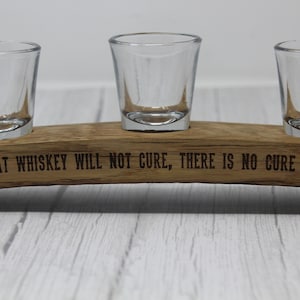 May include: A wooden shot glass holder with three shot glasses. The holder is engraved with the text "What whiskey will not cure, there is no cure for."