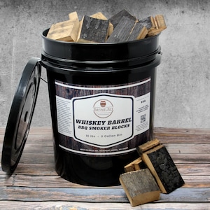 May include: A black 5-gallon bucket filled with whiskey barrel wood smoking blocks. The bucket has a label that reads "Whiskey Barrel BBQ Smoker Blocks" and "15 lbs - 5 Gallon Bin".
