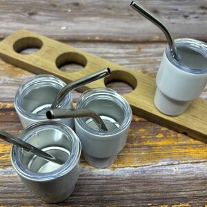 May include: Four white ceramic mugs with stainless steel straws. The mugs are sitting on a wooden tray with four holes.