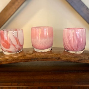 May include: Five pink and white votive candle holders with a marbled effect, displayed on a wooden wine barrel stave.