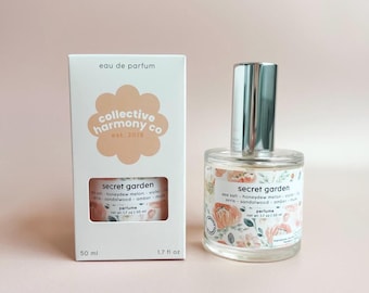 May include: A perfume bottle and box set. The clear glass bottle has a silver cap and a floral label that reads "Secret Garden." The box, labeled "eau de parfum," features the brand name and the words "Secret Garden."