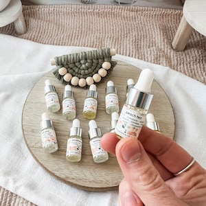 Może przedstawiać: Kolekcja małych szklanych butelek ze srebrnymi nakrętkami i etykietami. Butelki zawierają olejki eteryczne o różnych zapachach, w tym "Peach Tea", "Summer", "Sandalwood" i "Evergreen".