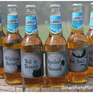 May include: Six glass bottles of Clipper Light beer with Halloween-themed labels. The labels feature spooky phrases like "Poison," "Witches Brew," and "Bat Juice," along with related graphics. The bottles are arranged on a wooden surface.
