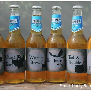 May include: Six glass bottles of Clipper Light beer with Halloween-themed labels. The labels feature spooky phrases like "Spider Venom," "Ghost Tears," and "Poison," with corresponding graphics. The bottles are arranged on a wooden surface.
