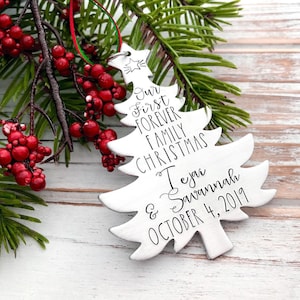 May include: A silver Christmas tree ornament with the text "Our First Forever Family Christmas Teja & Savannah October 4, 2019".