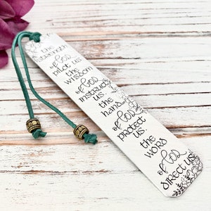 May include: A silver bookmark with a green leather strap and gold beads. The bookmark features a floral design and the text "the strength of God pilot us the wisdom of God instruct us. the hands of God protect us. the words of God direct us."