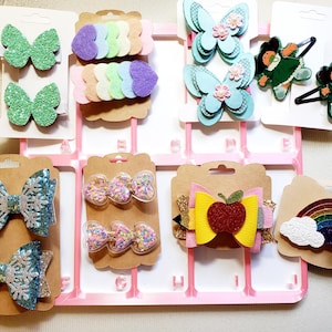 May include: A collection of colorful hair accessories, including glittery butterfly clips, felt bows, and sequined hair bows. The accessories are displayed on cardboard backing cards, perfect for gifting or retail display.