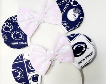 May include: White headband with two white bows and blue and white fabric mouse ears. The fabric has the Penn State Nittany Lion logo and other team graphics.