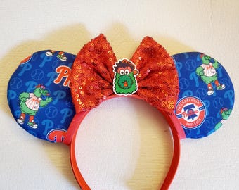 May include: Red sequin bow headband with a green and white Philadelphia Phillies character, a baseball logo, and the text "Philadelphia Phillies" on the blue fabric ear pieces.