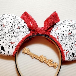 May include: A headband featuring two circular ears covered in a white fabric with a black and white dalmatian puppy print. A bright red sequined bow sits between the ears, accented with red braided trim. A wooden cutout reads WhimsyandWhatKnots.