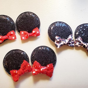 May include: Black sequined mouse ear headbands with red and leopard print bows. The red bows have white polka dots. The ears are round and the bows are centered on the ears. The headbands are for themed parties.