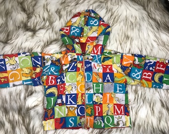 May include: A colorful hooded jacket with a zipper closure. The jacket is covered in a pattern of letters and illustrations from the book "The Cat in the Hat".