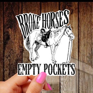 May include: A white sticker with black text that reads "Broke Horses Empty Pockets". A black and white illustration of a horse with a saddle is above the text.