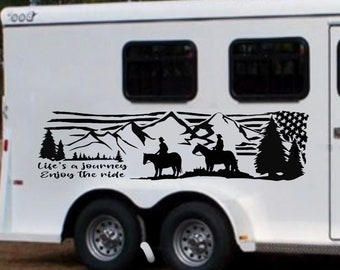 以下が含まれることがあります： 2頭の馬に乗ったライダーが描かれた山岳風景の黒いシルエットのステッカーが貼られた白い馬運搬車。ステッカーには「Life's a journey, Enjoy the ride」というテキストが書かれています。