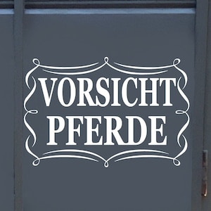 May include: A gray horse trailer with a white warning sign that reads "Vorsicht Pferde" in a decorative font.