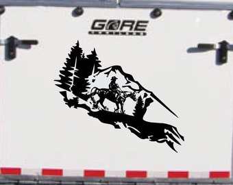 May include: A white horse trailer with a black silhouette decal of a rider on horseback in a mountain landscape. The decal includes trees and a mountain range. The trailer has the word "GORE" printed on the back.