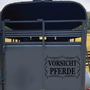 May include: A gray horse trailer with a black warning sign that reads "Vorsicht Pferde" which translates to "Caution Horses" in English.