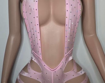May include: A pink halter-style bodysuit with a plunging neckline and cutouts on the sides. The bodysuit is covered in rhinestones.