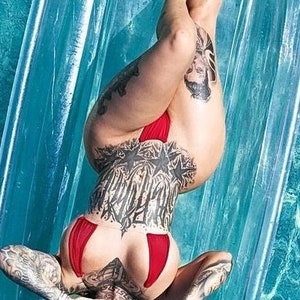 May include: A woman with tattoos lies on her back in a swimming pool, wearing a red bikini top and bottom. The water is blue and the pool is lined with white tiles.