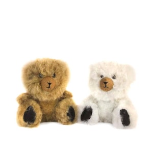 May include: Two plush teddy bears. One is light brown, the other is white. Both have brown noses and black paw pads. The bears are sitting upright against a white background. The fur is soft and fluffy.