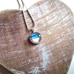 May include: A silver chain necklace with a round pendant featuring a blue, white, and pink abstract design.