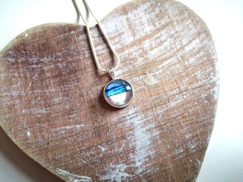 May include: A silver chain necklace with a round pendant featuring a blue, white, and pink abstract design.