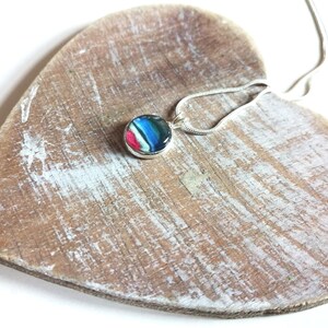 May include: A silver chain necklace with a round pendant featuring a colorful abstract design. The pendant is made of resin and has a glossy finish.