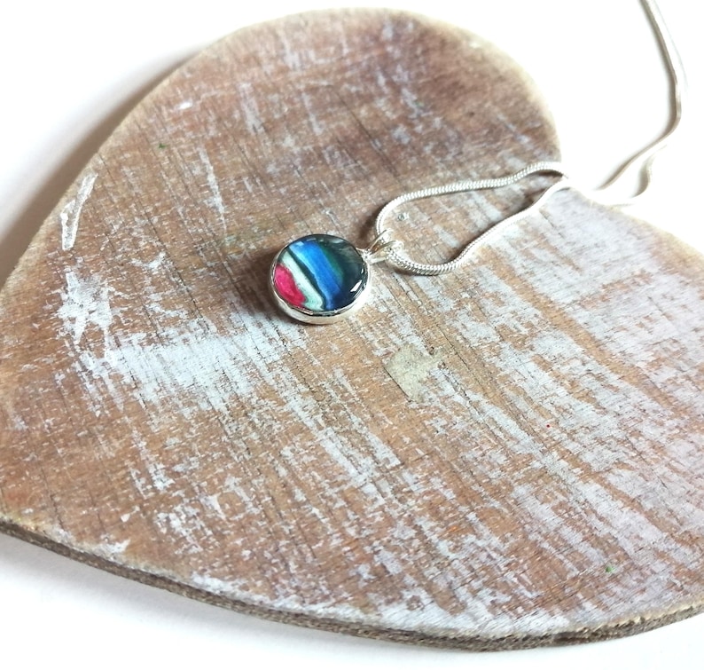 May include: A silver chain necklace with a round pendant featuring a colorful abstract design. The pendant is made of resin and has a glossy finish.