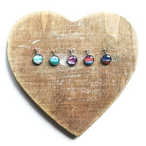 May include: Five small round pendants with different colourful striped designs. The pendants are on a wooden heart-shaped surface.