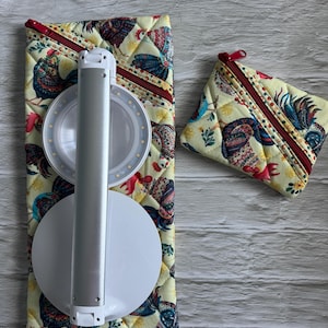 Pode incluir: Uma lâmpada de mesa LED prateada e branca é exibida em uma capa de tecido amarelo acolchoado com um padrão de galo. Uma pequena bolsa com zíper combinando também é visível. O padrão do galo inclui detalhes em vermelho, azul e verde.