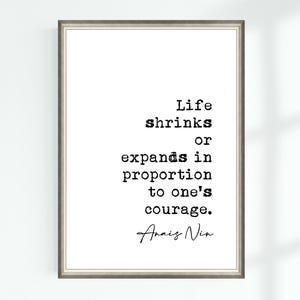 May include: A framed print featuring a quote in black text on a white background. The quote reads, "Life shrinks or expands in proportion to one's courage." The author's name, Anais Nin, is below. The frame is a grey colour.