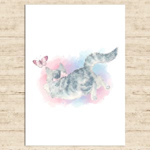 May include: Watercolor print of a playful cat with gray and white fur, reaching for a pink butterfly. The cat is set against a soft background of pink and blue watercolor washes, creating a whimsical scene.