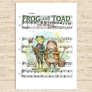 May include: A whimsical print featuring musical notes and the words "FROG AND TOAD THE MUSICAL." The artwork depicts two anthropomorphic frogs in formal attire, surrounded by teacups, a snail, and a basket of cookies, set against a watercolor background.