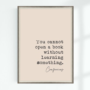 May include: A framed print featuring a quote by Confucius: "You cannot open a book without learning something." The text is in black against a light beige backdrop. The frame is a muted grey.