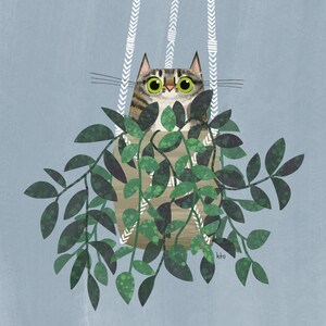 以下が含まれることがあります： 緑色の目をしたトラ猫が、緑の葉でいっぱいの吊り下げられたプランターから顔を出しています。プランターは白と茶色の模様の織り素材で作られています。