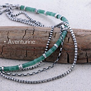 Op de afbeelding: Een meerrijige ketting met een streng groene, cilindervormige aventurijnkralen en zilverkleurige metalen tussenstukjes, gecombineerd met twee verschillende zilverkleurige metalen kettingen. De tekst "Aventurine" is links zichtbaar.
