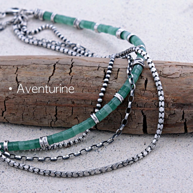 May include: A multi-strand necklace featuring green aventurine cylindrical beads accented with silver-toned metal spacers and various silver-toned chain links. The word Aventurine is printed in white text on the left side of the image.